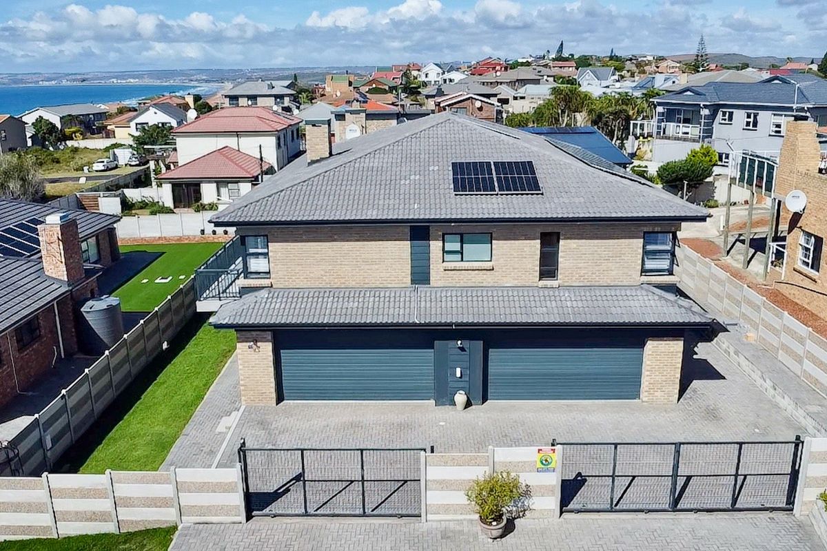 Aerial view of a modern double-story house featuring a double garage, paved driveway, secure boundary wall, and solar panels on a tiled roof.