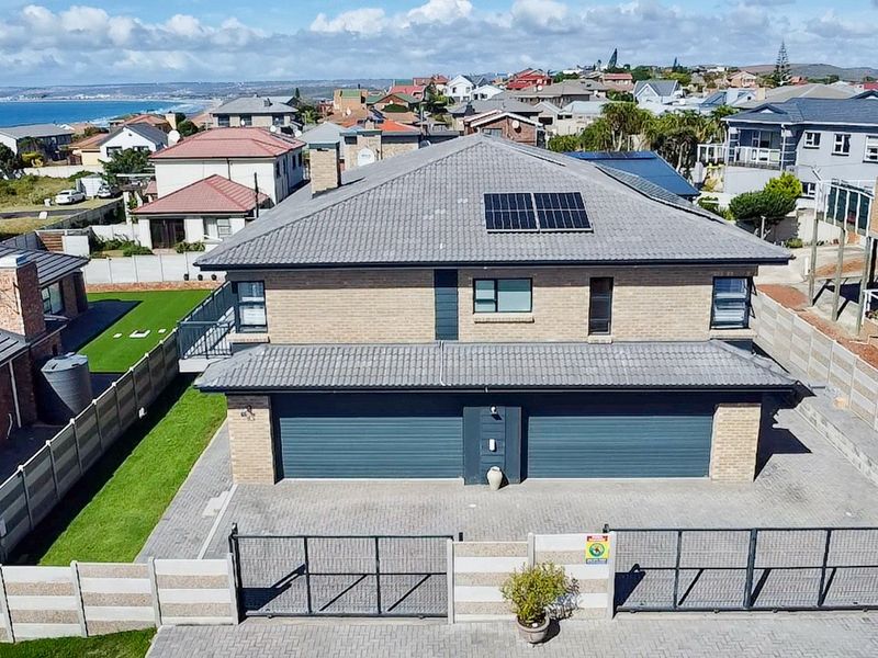 Aerial view of a modern double-story house featuring a double garage, paved driveway, secure boundary wall, and solar panels on a tiled roof.