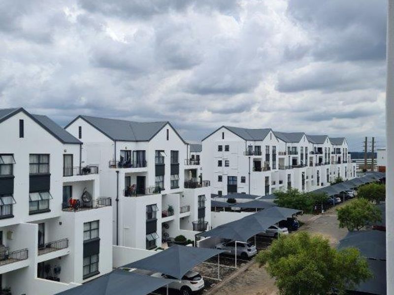 An elevated view of a modern apartment complex featuring white facades, private balconies, and covered parking bays with shade cloth structures.