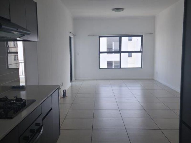 Spacious open-plan living area featuring a modern kitchen with built-in appliances, tiled flooring, and large windows providing ample natural light.