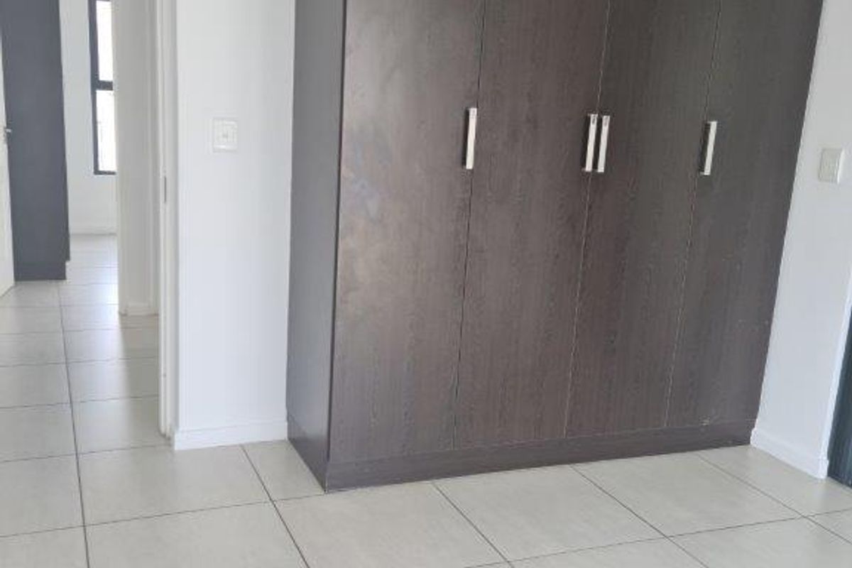 A bright, empty bedroom featuring modern dark wood built-in cupboards and neutral tiled flooring, offering a clean and versatile living space.