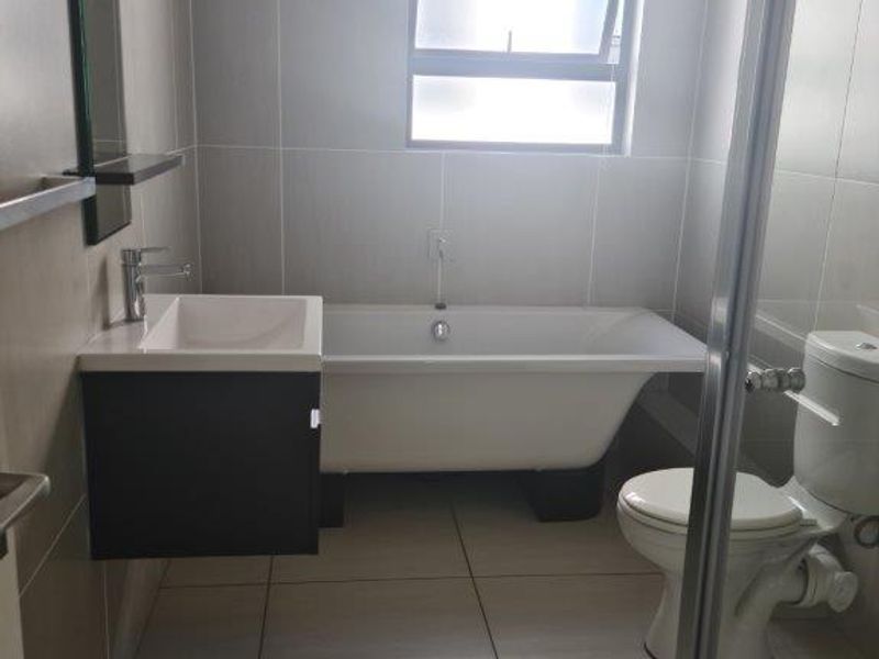 A modern, clean bathroom featuring a freestanding bathtub, wall-mounted vanity with basin, and a toilet, finished with neutral floor-to-ceiling wall tiles.