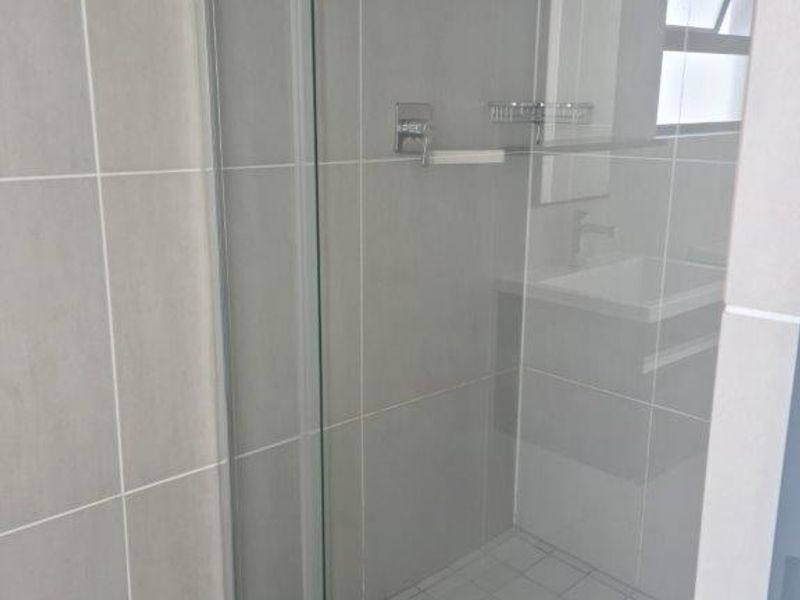 A modern bathroom featuring a glass-enclosed shower with tiled walls and a vanity basin with cabinet storage.
