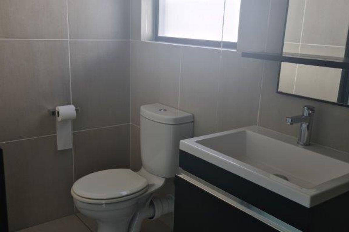 A modern, clean bathroom featuring a wall-mounted vanity with a basin, a toilet, and neutral floor-to-ceiling tiling.