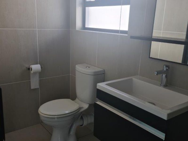 A modern, clean bathroom featuring a wall-mounted vanity with a basin, a toilet, and neutral floor-to-ceiling tiling.