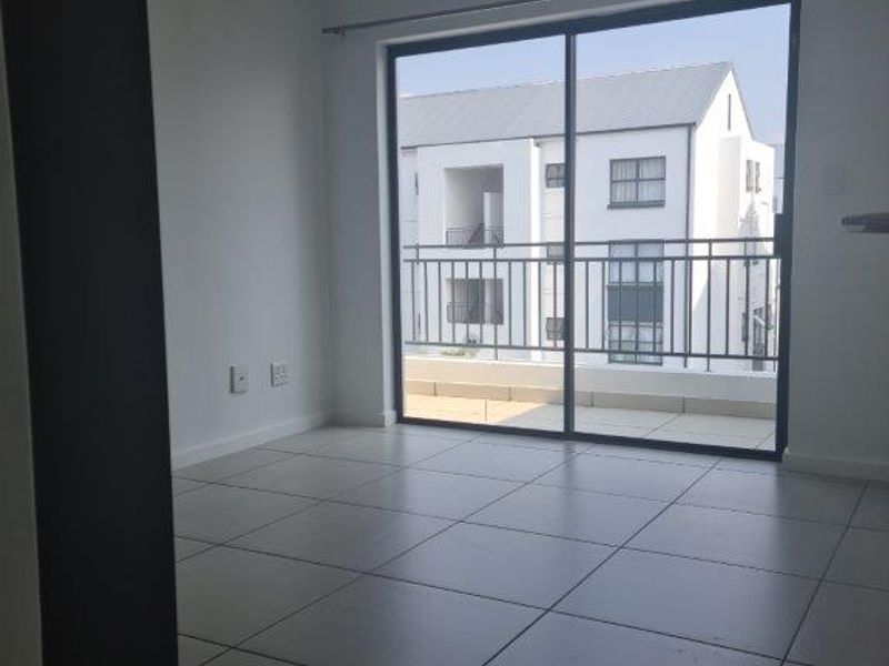 An empty, well-lit living area featuring neutral tiled flooring and a large sliding glass door providing direct access to a private balcony.