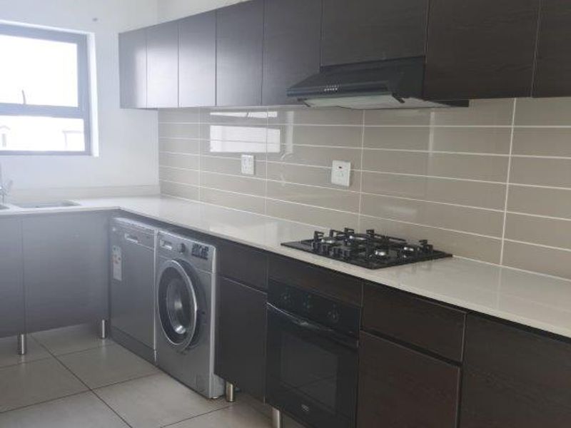 Modern kitchen featuring dark wood cabinetry, stone countertops, subway tile backsplash, and integrated appliances including a gas hob, oven, and extractor fan.