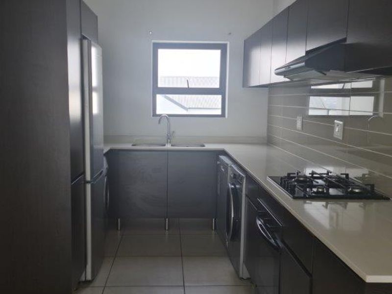 A modern kitchen featuring dark cabinetry, stone countertops, a gas hob with extractor fan, and tiled flooring with a neutral backsplash.