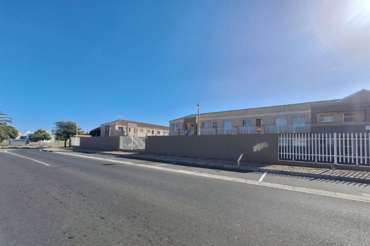 Street view of the apartment complex featuring a perimeter wall, security fencing, and paved road access.