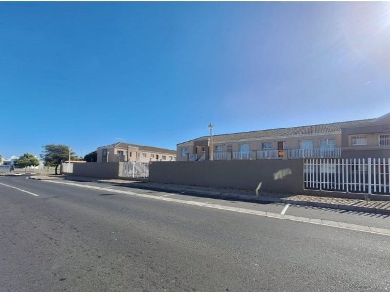 Street view of the apartment complex featuring a perimeter wall, security fencing, and paved road access.