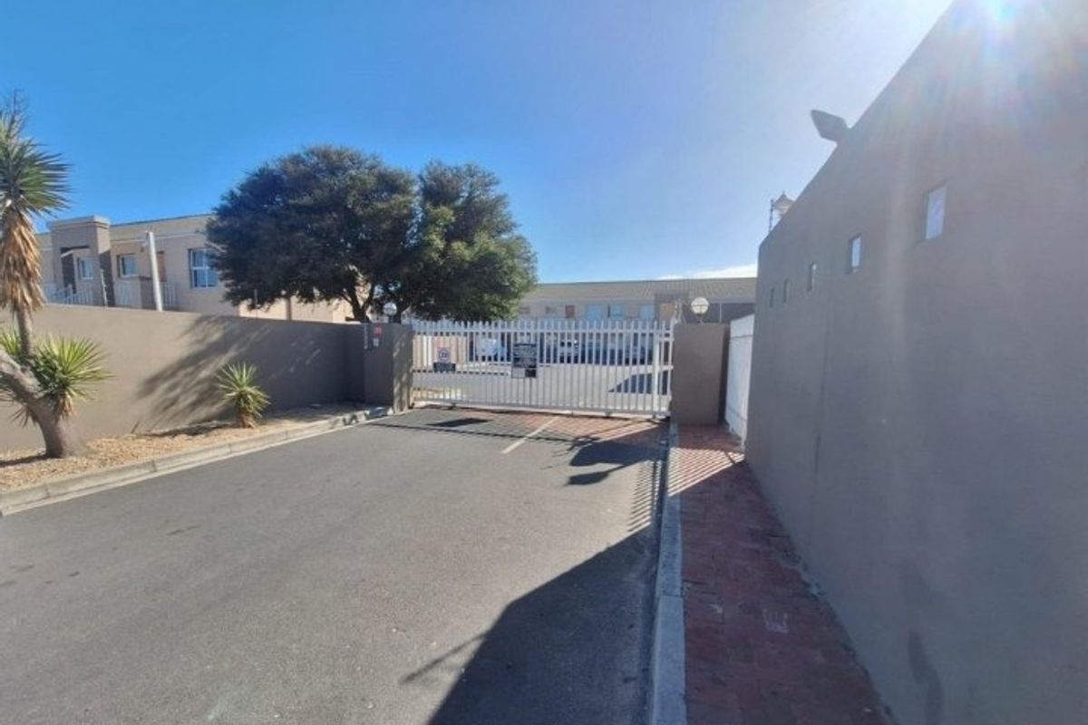 The entrance to the apartment complex features a secure gated access point with perimeter walls and paved driveway.
