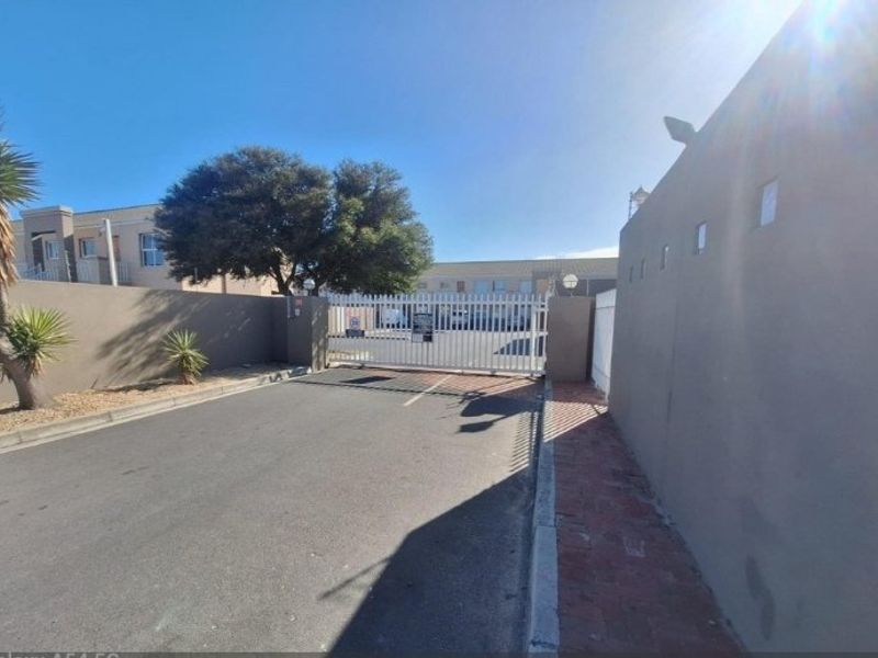 The entrance to the apartment complex features a secure gated access point with perimeter walls and paved driveway.