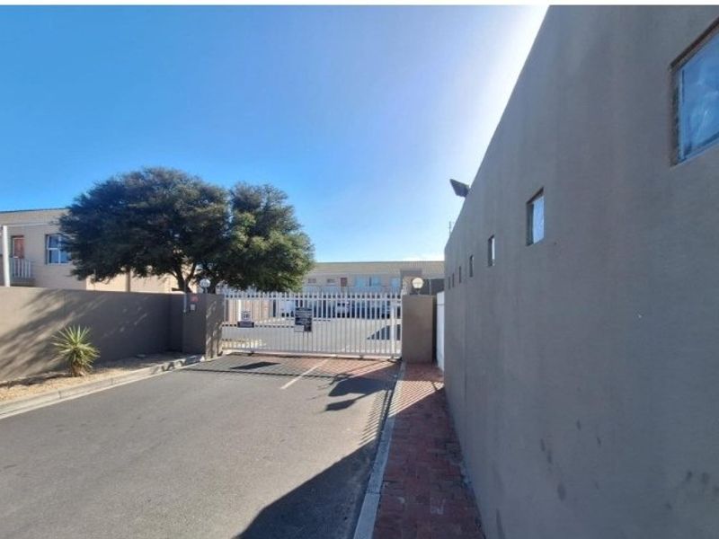 View of the apartment complex entrance featuring a secure gated access point, boundary walls, and paved driveway.