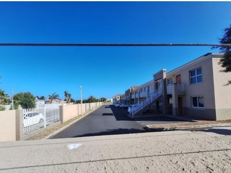 Exterior view of the apartment complex featuring a paved driveway, parking area, and external staircase access to upper-level units.