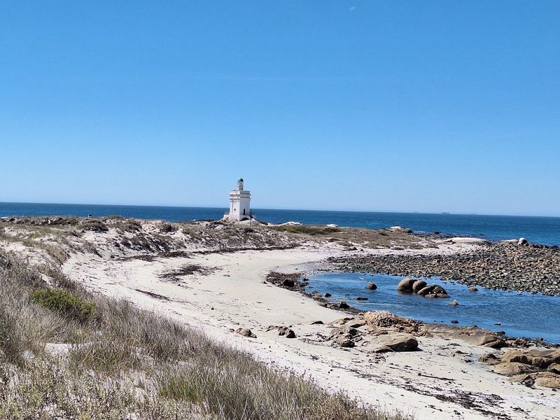 A scenic coastal view featuring a lighthouse situated on a rocky shoreline overlooking the ocean and sandy beach.