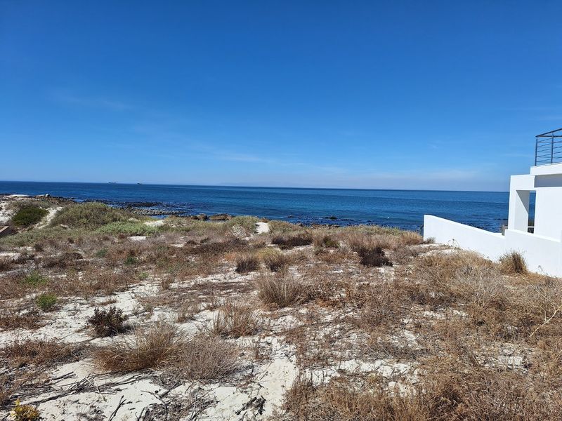 A scenic view of the ocean from a vacant residential plot featuring natural coastal vegetation and a partial view of an adjacent structure.