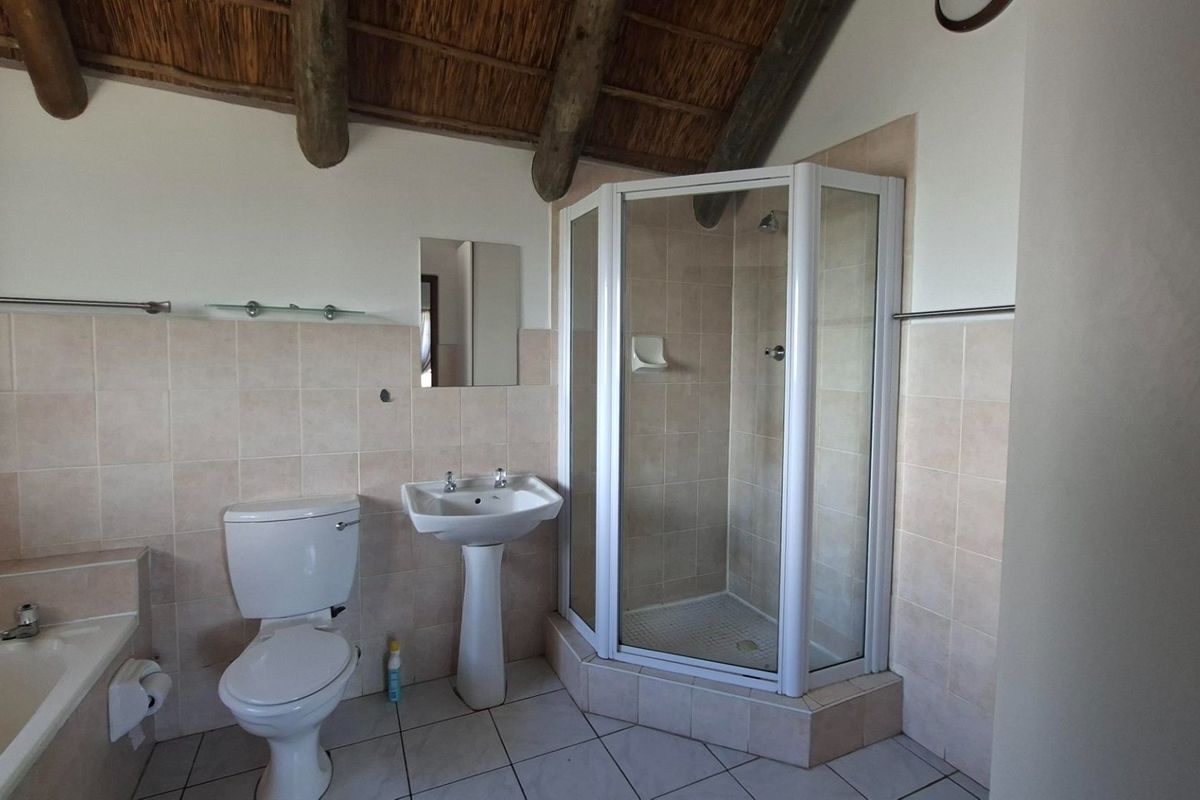 A functional bathroom featuring a corner shower, pedestal basin, and built-in bathtub, complemented by a unique thatched ceiling with exposed timber rafters.
