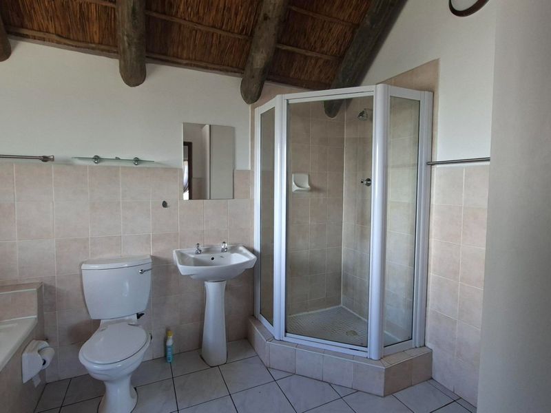 A functional bathroom featuring a corner shower, pedestal basin, and built-in bathtub, complemented by a unique thatched ceiling with exposed timber rafters.