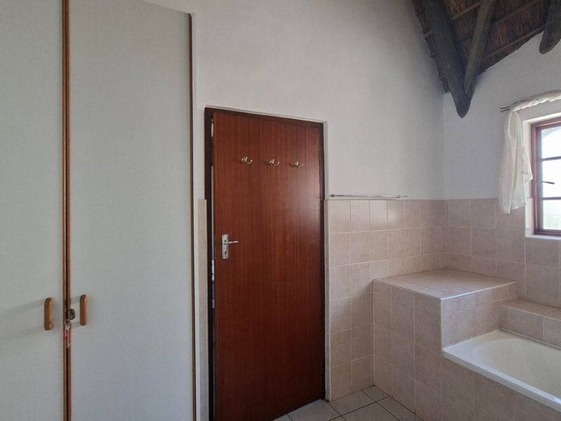 A functional bathroom featuring built-in cupboards, a tiled bathtub surround, and exposed timber roof trusses, offering a clean and practical layout.