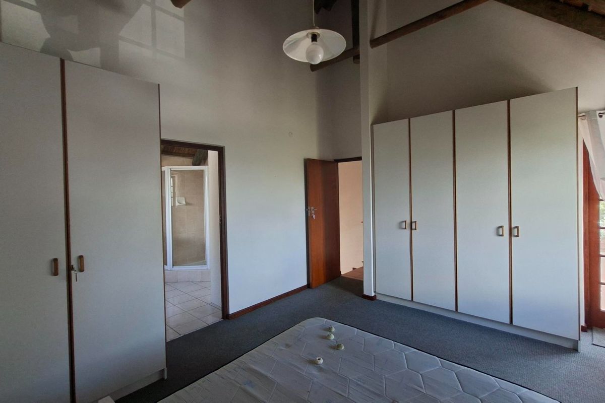 Spacious bedroom featuring built-in cupboards, exposed timber ceiling beams, carpeted flooring, and direct access to an en-suite bathroom and outdoor area.