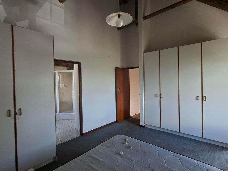 Spacious bedroom featuring built-in cupboards, exposed timber ceiling beams, carpeted flooring, and direct access to an en-suite bathroom and outdoor area.