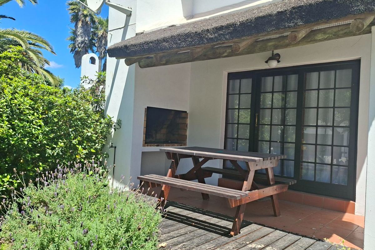 Covered patio area featuring a built-in braai, tiled flooring, and timber decking, providing a functional outdoor entertainment space.
