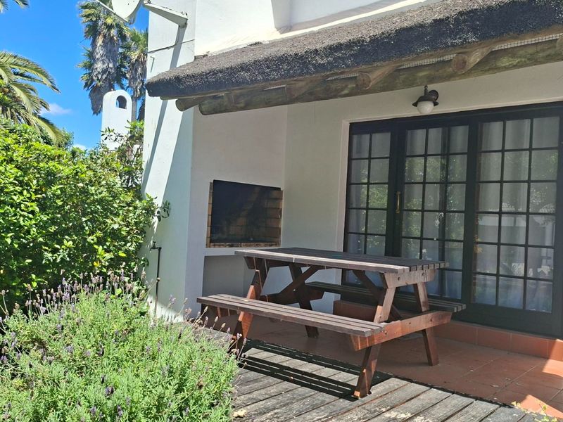 Covered patio area featuring a built-in braai, tiled flooring, and timber decking, providing a functional outdoor entertainment space.