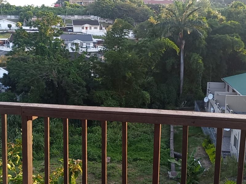 A balcony with a wooden balustrade offering an elevated view of the surrounding neighborhood and lush greenery.