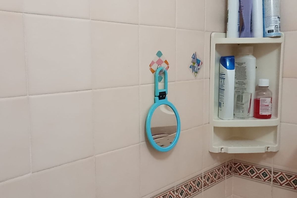 A close-up view of a bathroom wall featuring light-colored ceramic tiles, a decorative border, and a built-in corner storage shelf.