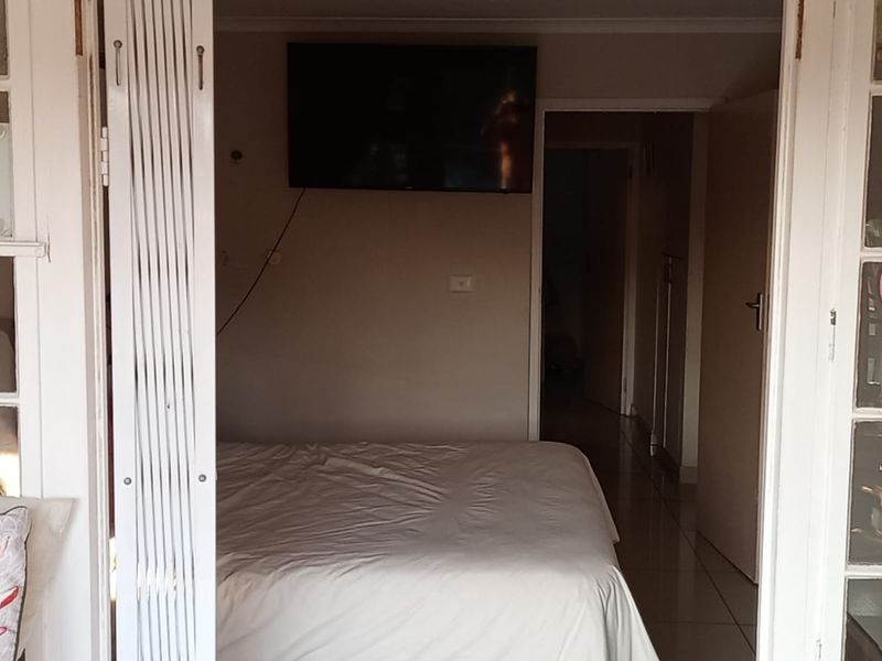 A bedroom featuring tiled flooring and access through classic french doors, leading into a hallway area.