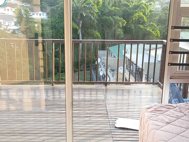 A wooden balcony featuring timber decking and a balustrade, accessible via a sliding glass door, offering an elevated view of the surrounding neighborhood.