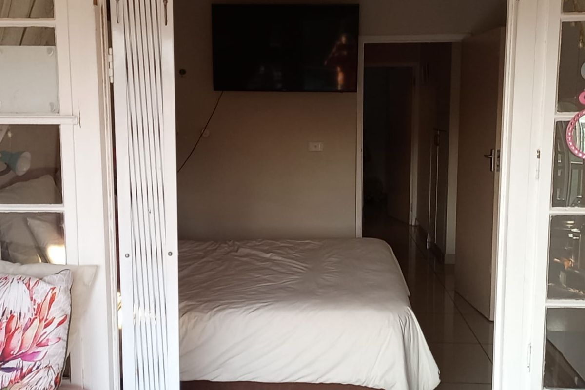 A bedroom featuring tiled flooring and access via white-framed french doors, with a wall-mounted television and neutral wall finishes.