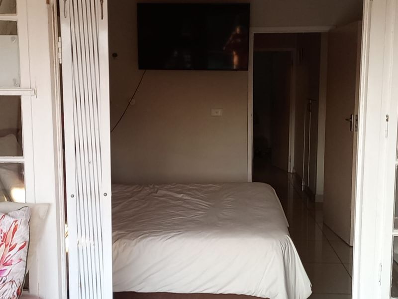 A bedroom featuring tiled flooring and access via white-framed french doors, with a wall-mounted television and neutral wall finishes.