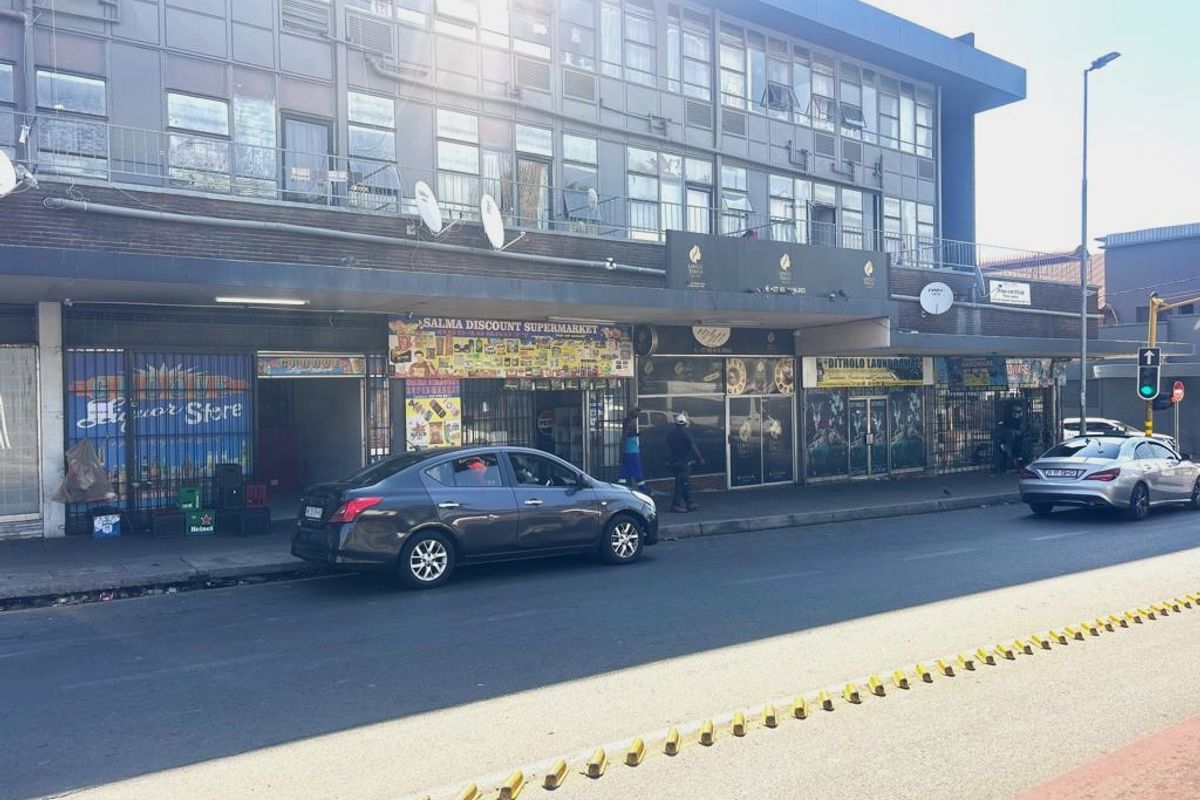 A multi-level commercial building featuring ground-floor retail storefronts with security gates and upper-level office or residential windows along a busy street.