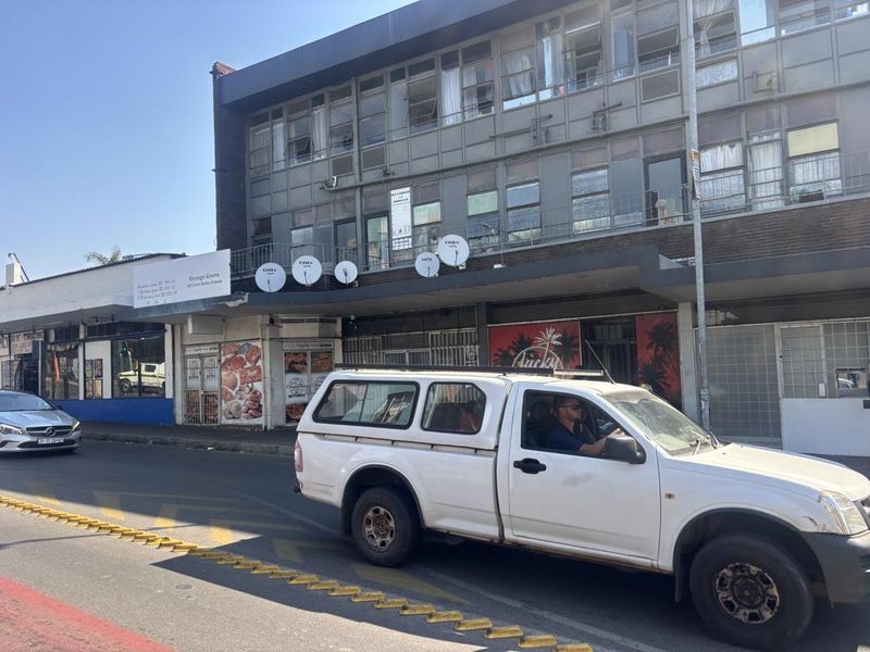 Street-level view of a multi-story commercial building featuring ground-floor retail shopfronts and upper-level office or residential windows with multiple satellite dishes.
