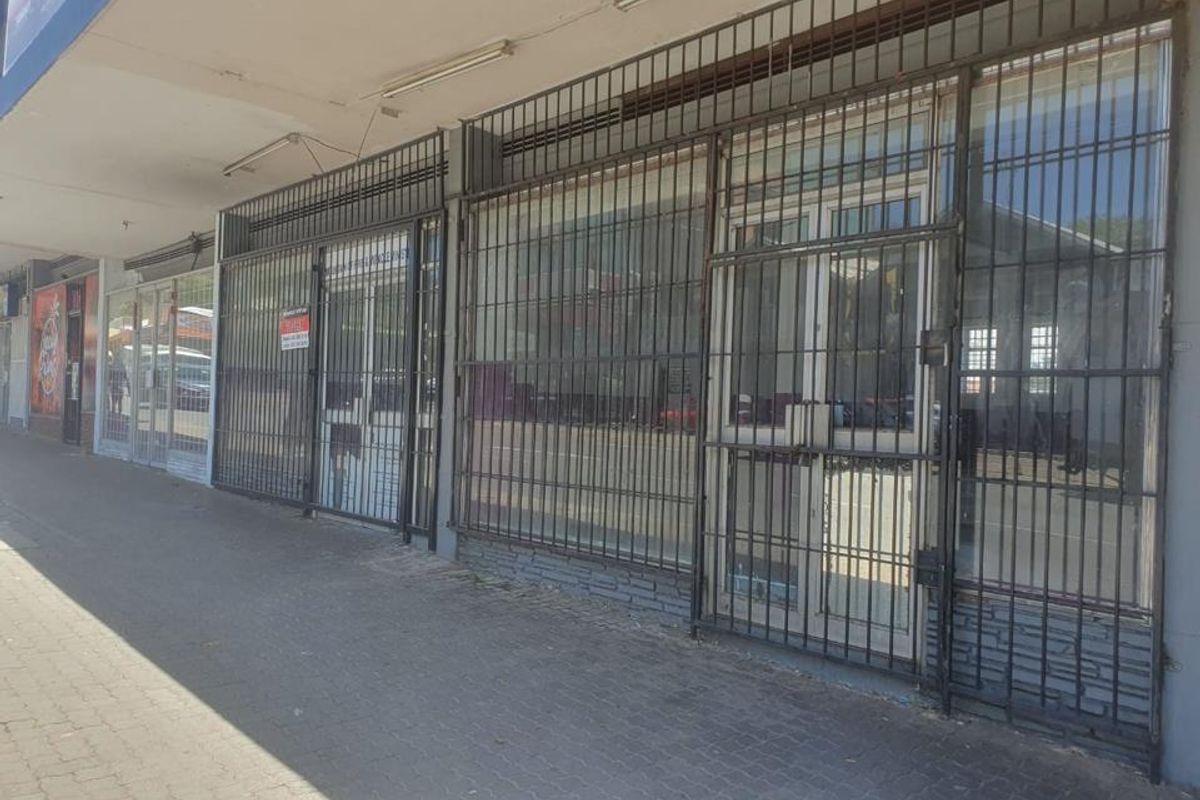 Commercial storefront featuring large glass windows protected by security bars, situated along a paved sidewalk with overhead lighting.