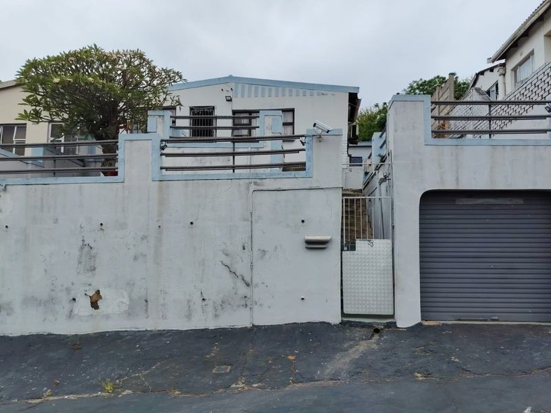 Front elevation of the property featuring a garage, security gate, and boundary wall with visible signs of wear and maintenance requirements.