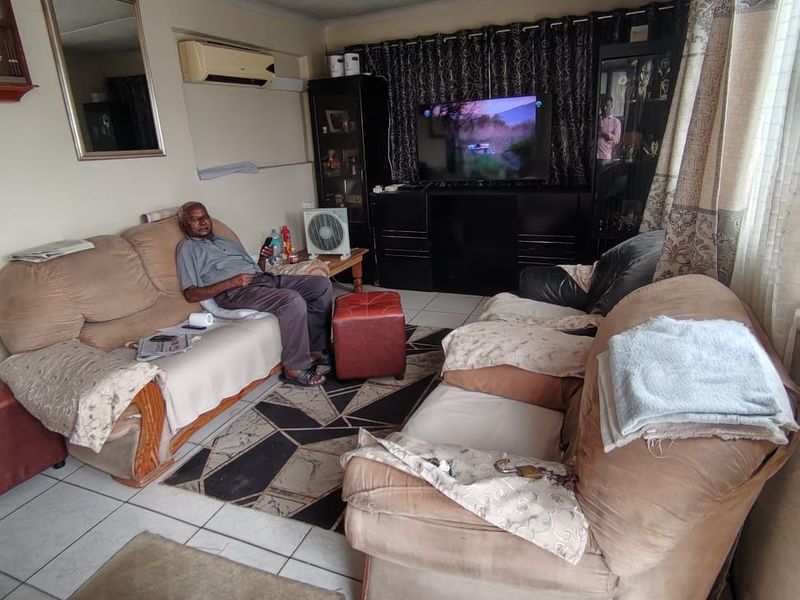 A living room featuring tiled flooring, a wall-mounted air conditioning unit, and built-in cabinetry, offering a functional space with potential for cosmetic updates.