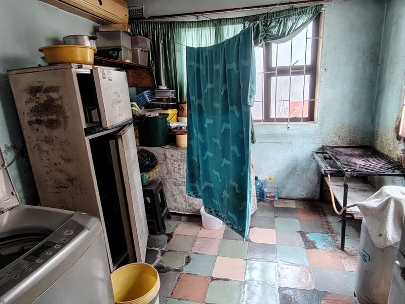 A laundry area featuring tiled flooring, security bars on the window, and a wall-mounted air conditioning unit, currently requiring significant ceiling and wall repairs.