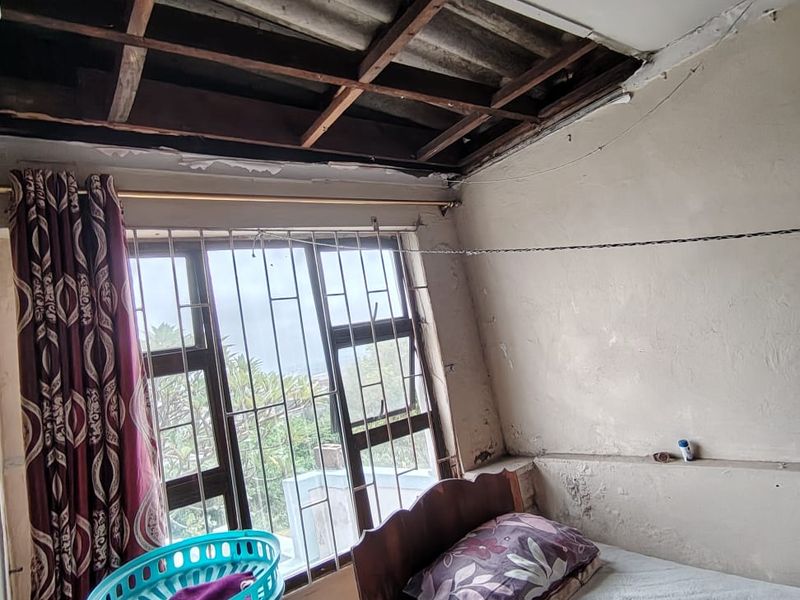 A bedroom featuring security bars on the window and significant ceiling damage with exposed rafters, requiring structural repair and cosmetic renovation.