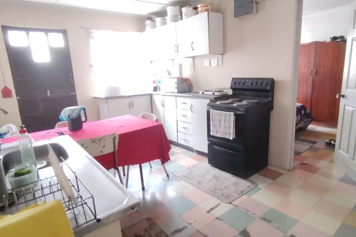 A dated kitchen featuring original cabinetry, a freestanding stove, and multi-colored tiled flooring in need of renovation.