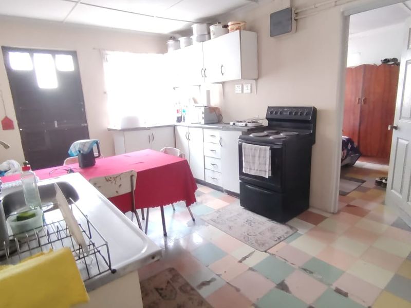 A dated kitchen featuring original cabinetry, a freestanding stove, and multi-colored tiled flooring in need of renovation.