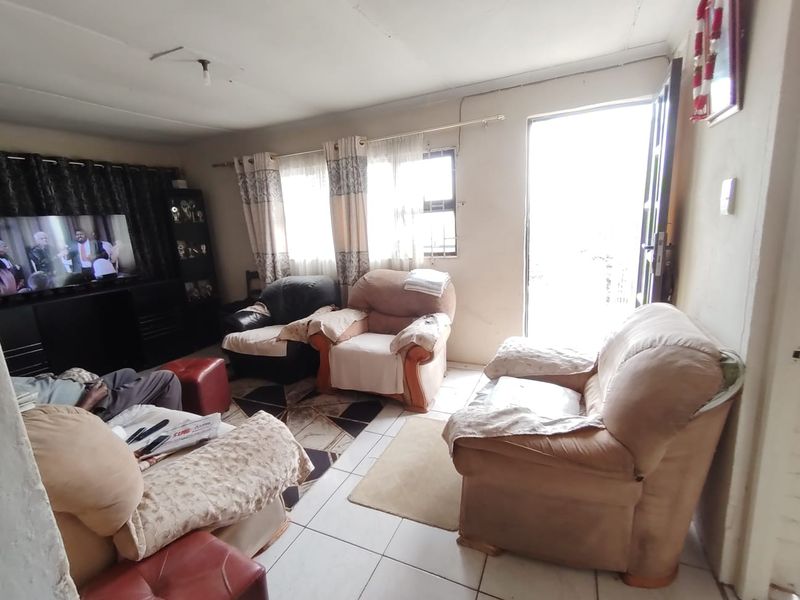 A living room featuring tiled flooring and natural light from windows and an external door, requiring cosmetic updates to improve the overall finish.