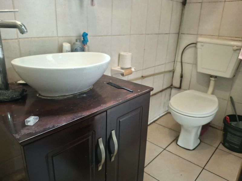 A functional bathroom featuring a vessel sink on a vanity cabinet, a standard toilet, and tiled walls and flooring.