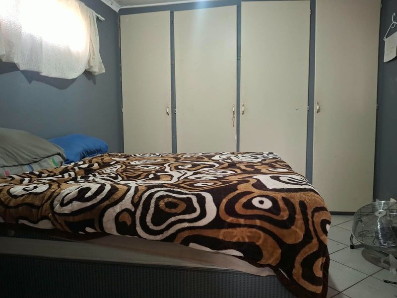 A bedroom featuring built-in cupboards and tiled flooring, offering a functional space with potential for cosmetic updates.