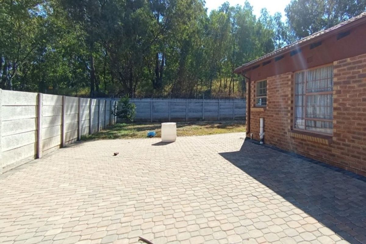 A rear exterior view featuring a paved patio area, brick building facade, and a secure precast concrete boundary wall.