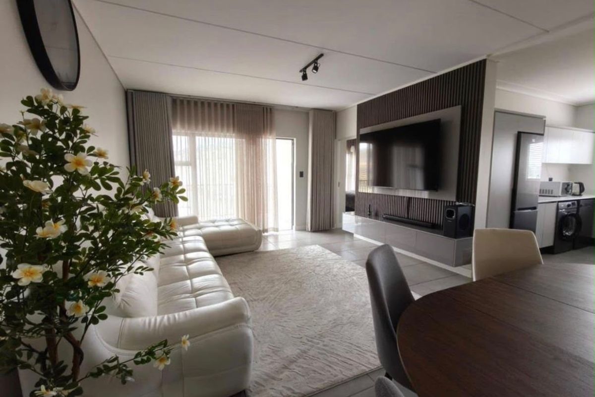 Modern open-plan living area featuring a stylish slatted wood feature wall with integrated media console, tiled floors, and seamless flow to the kitchen.