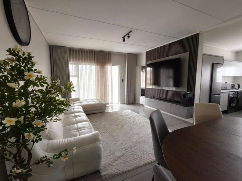 Modern open-plan living area featuring a stylish slatted wood feature wall with integrated media console, tiled floors, and seamless flow to the kitchen.
