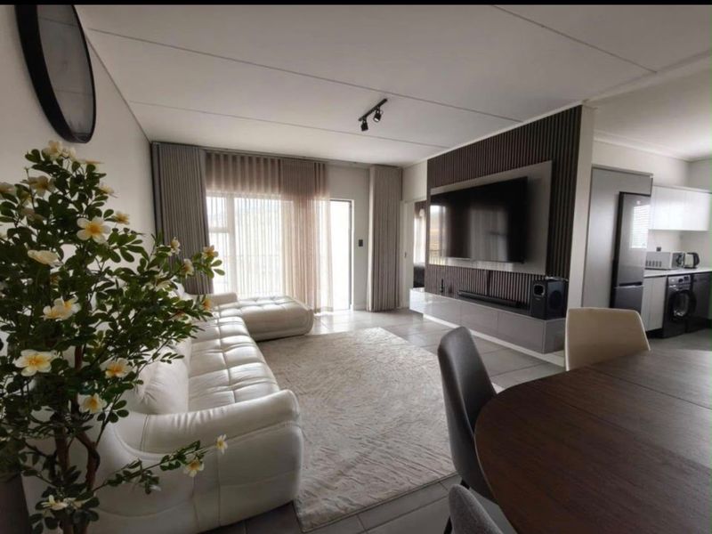 Modern open-plan living area featuring a stylish slatted timber feature wall with integrated media console, tiled floors, and seamless flow into the kitchen.