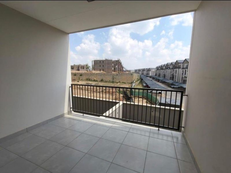 A clean, covered balcony featuring tiled flooring and a metal balustrade, offering an open view of the surrounding residential complex.